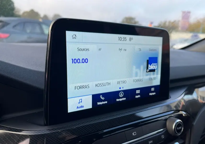 Écran tactile central du Ford Kuga 2022 affichant la radio, avec tableau de bord noir et finition carbone.