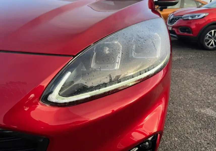 Gros plan sur le phare avant gauche du Ford Kuga rouge Lucifer 2022 avec gouttes d'eau et calandre partielle visible.