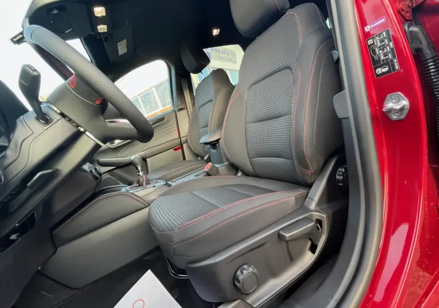 Vue intérieure côté conducteur du Ford Kuga rouge Lucifer 2022, sièges tissu noirs avec surpiqûres rouges et volant sport.