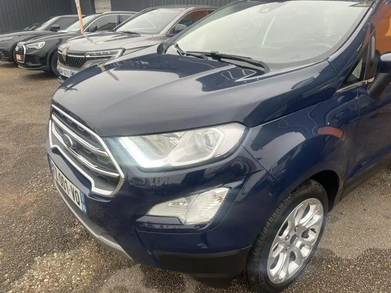 Vue 3/4 avant droit d'un Ford EcoSport 1.0 EcoBoost Titanium Bleu Abysse avec calandre chromée et phares allumés.