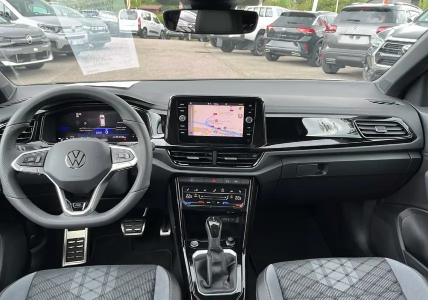Intérieur du Volkswagen T-Roc 2025 gris indium, vue du poste de conduite avec écran tactile et volant multifonctions.