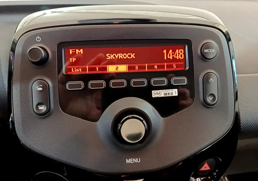 Vue rapprochée de la radio digitale rouge allumée dans le tableau de bord noir de la Citroën C1 blanche de 2020.