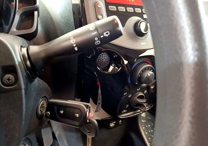 Gros plan sur le tableau de bord noir et la commande de climatisation de la Citroën C1 blanche, avec clé insérée.