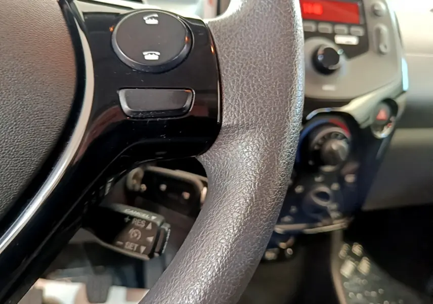 Gros plan sur le volant noir et les commandes intégrées, avec le tableau de bord flou en arrière-plan dans une Citroën C1.