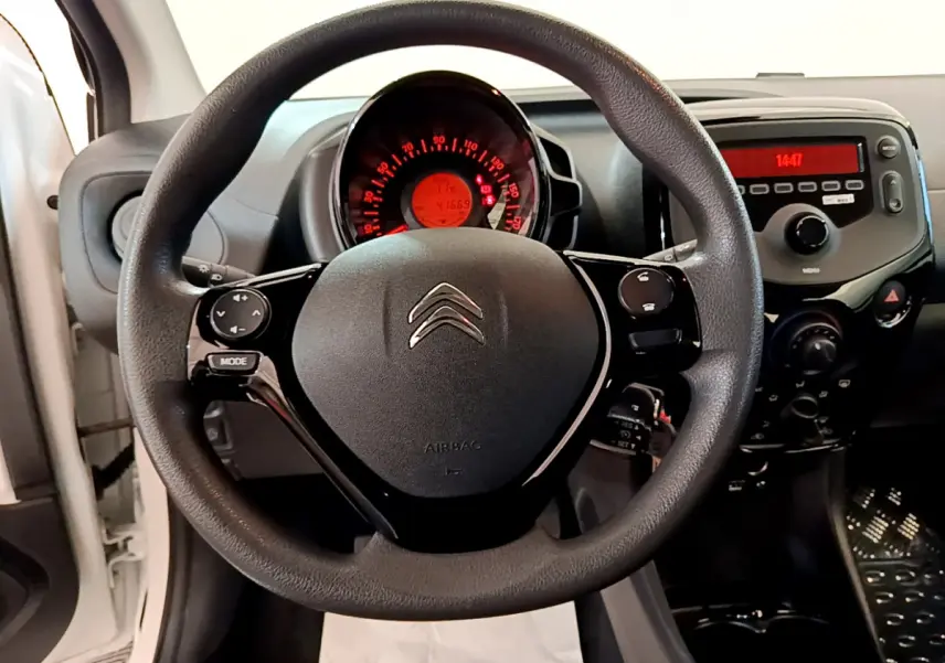 Vue intérieure centrée sur le volant noir de la Citroën C1 blanche, avec tableau de bord et commandes visibles.