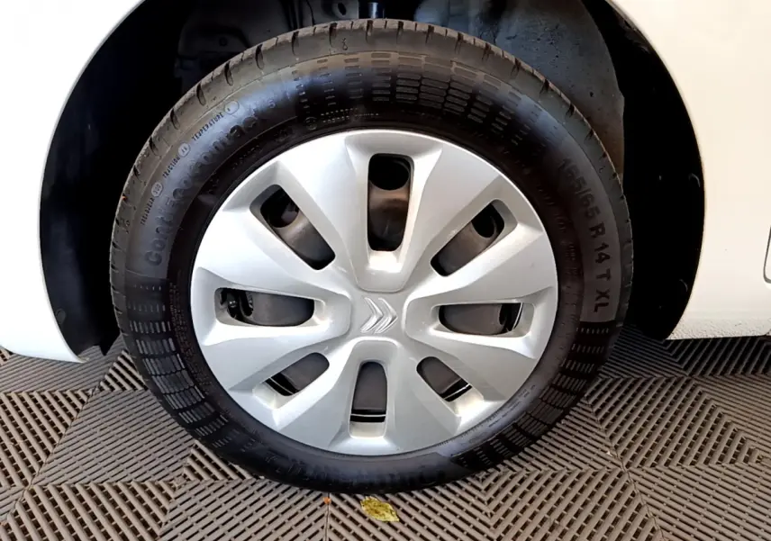 Gros plan sur la roue avant droite d'une Citroën C1 blanche avec enjoliveur argenté et logo Citroën central.