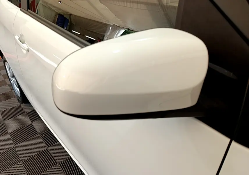 Gros plan sur le rétroviseur côté droit blanc d'une Citroën C1 blanche, avec une partie de la porte visible.