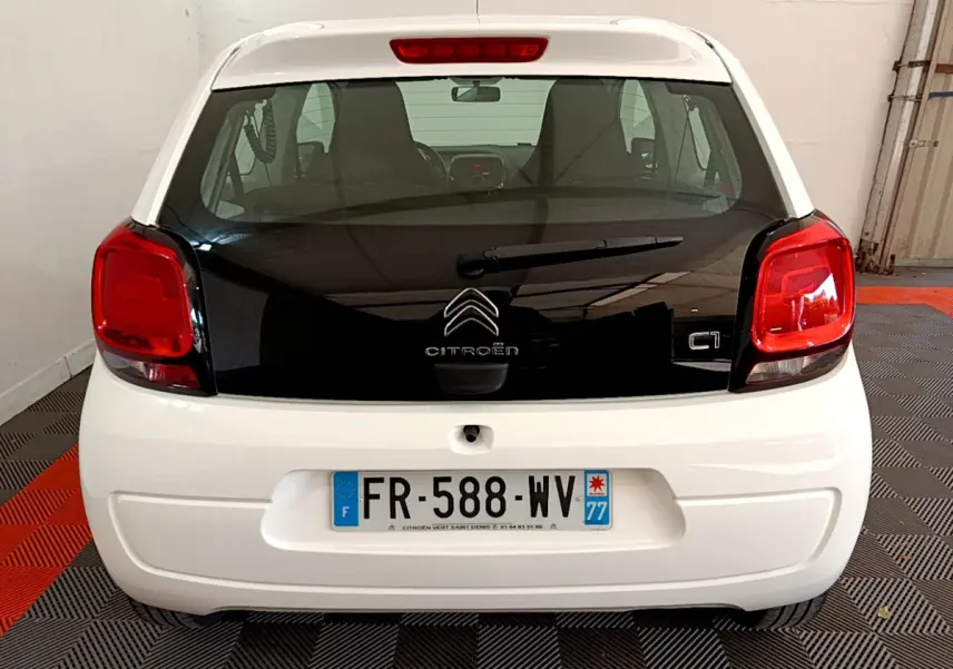 Vue arrière d'une Citroën C1 blanche avec hayon noir et feux arrière rouges dans un garage.