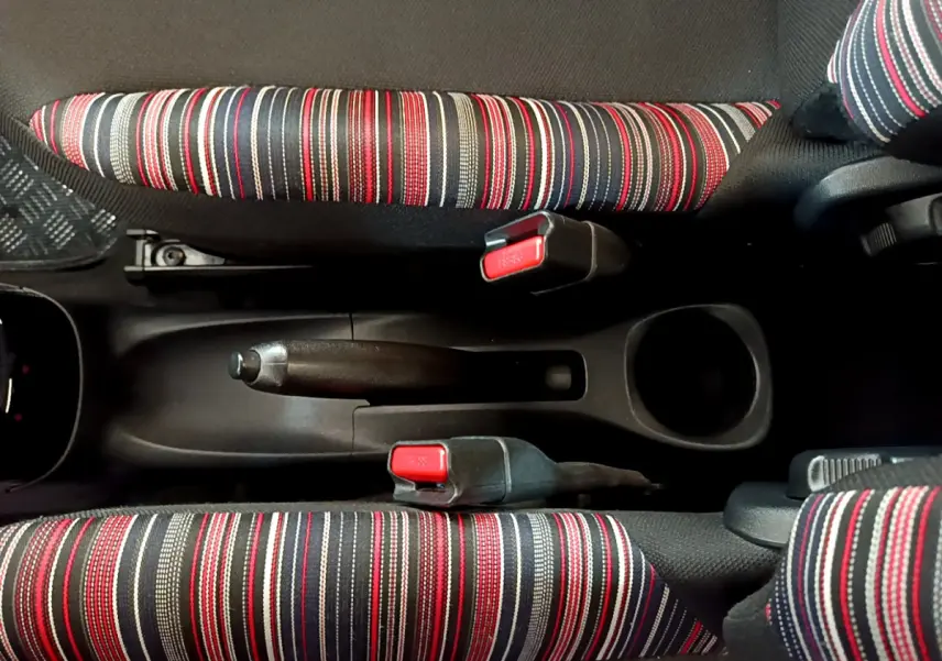 Vue plongeante sur la console centrale de la Citroën C1 2020, montrant les ceintures rouges et noires à rayures et le frein à main noir.