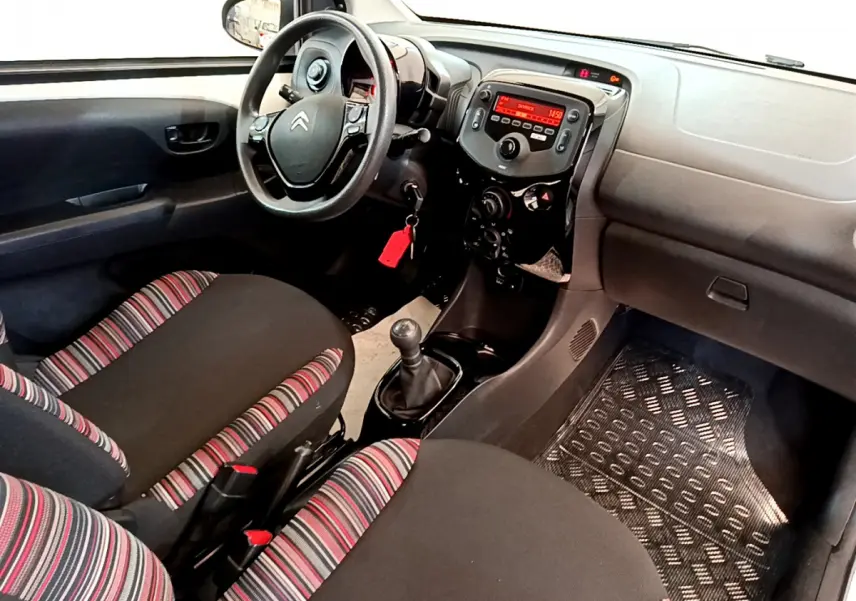 Vue intérieure avant droite du Citroën C1 2020, volant noir, sièges tissu rayé rouge et noir, console centrale avec radio.