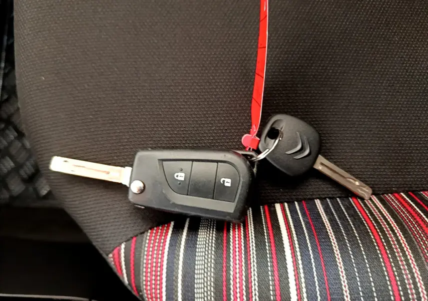 Clé de voiture Citroën posée sur un siège tissu noir avec bandes rouges, blanches et grises, vue rapprochée intérieure.