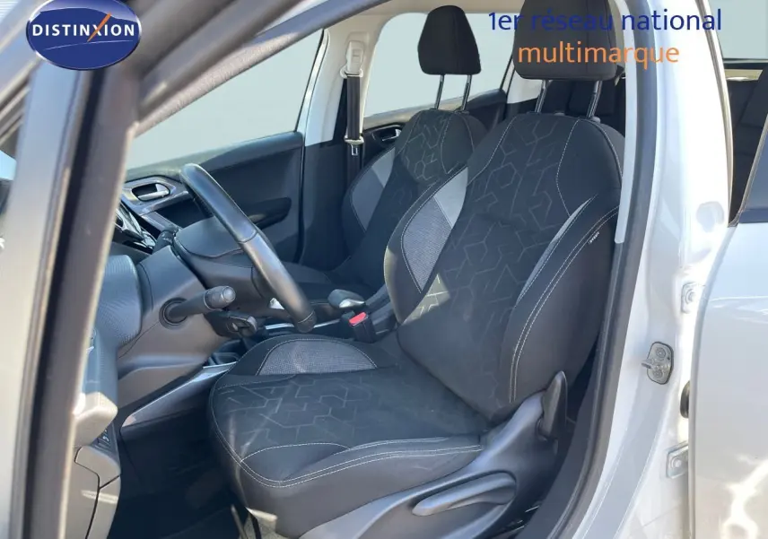 Vue intérieure côté conducteur d'une Peugeot 2008 blanche de 2017, sièges tissu gris noir avec motifs géométriques.