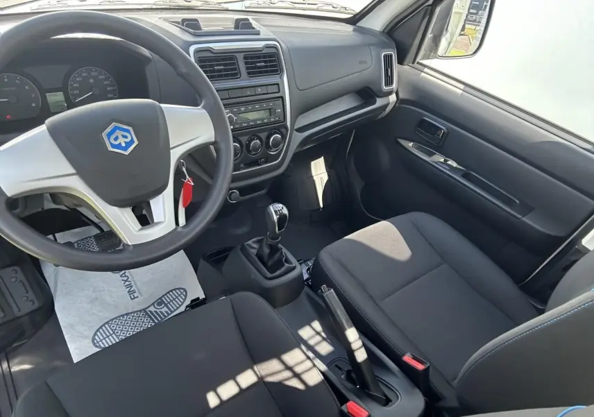Intérieur du Piaggio Porter 2024 vu côté conducteur, volant avec logo bleu, tableau de bord simple et sièges noirs.