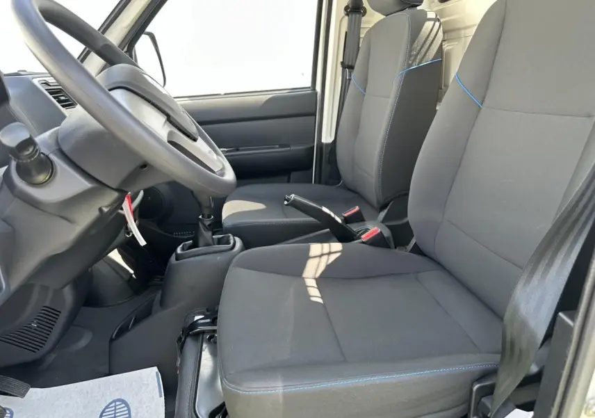 Intérieur du Piaggio Porter 2024 vu côté conducteur, sièges gris avec surpiqûres bleues et volant noir.