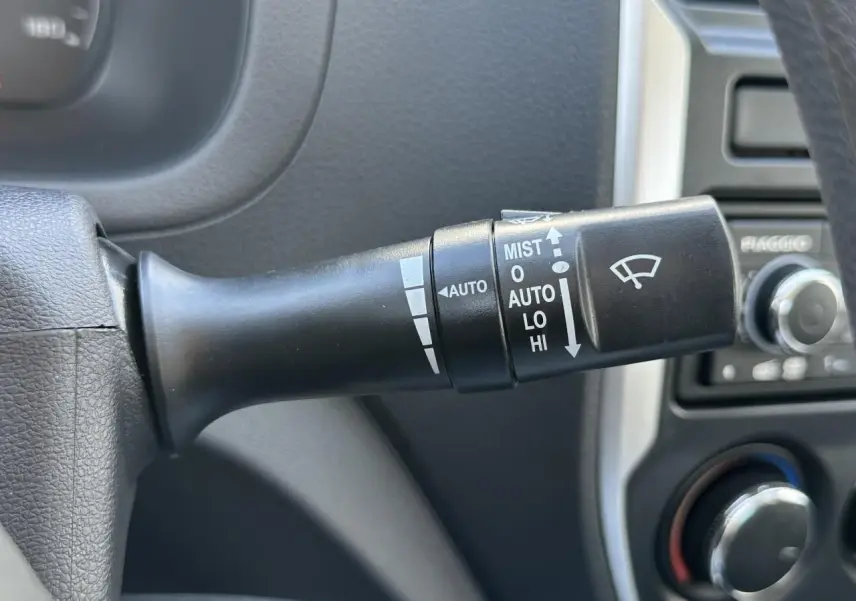 Gros plan sur la commande d'essuie-glace du Piaggio Porter blanc, avec tableau de bord et radio en arrière-plan.