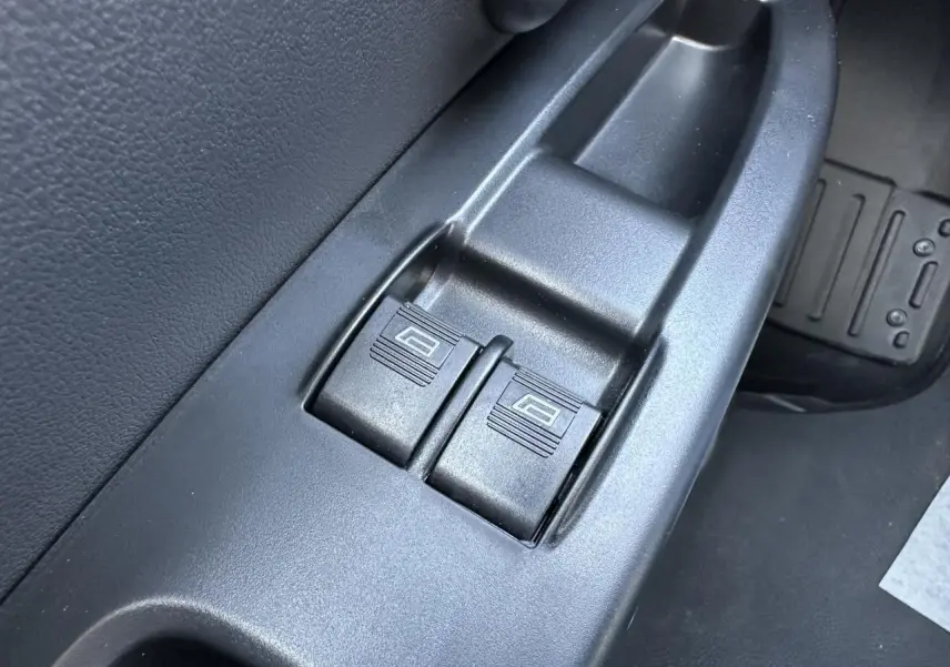 Gros plan sur les commandes de lève-vitres électriques côté conducteur du Piaggio Porter blanc, intérieur noir.