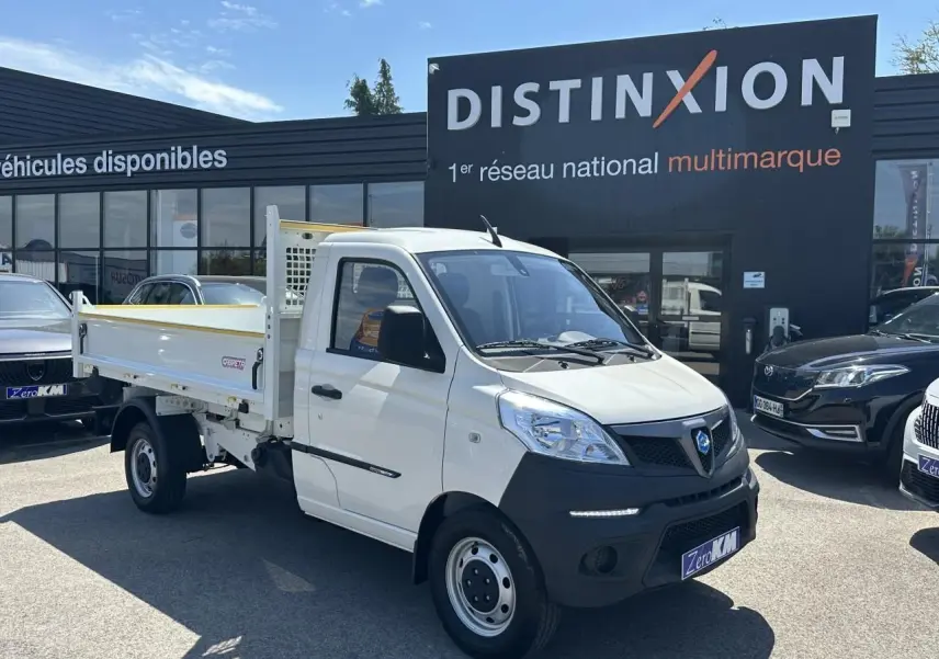 Vue 3/4 avant droite d'un Piaggio Porter blanc avec benne longue, stationné devant un concessionnaire multimarque.