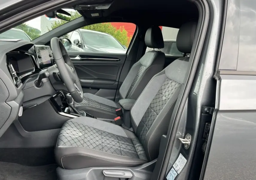 Vue intérieure côté conducteur du Volkswagen T-ROC gris indium 2025, sièges R-Line Black en cuir et alcantara avec surpiqûres.