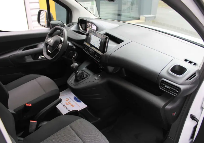 Intérieur du Peugeot Partner Fourgon 2025 vu côté conducteur, tableau de bord noir avec écran tactile et boîte manuelle.