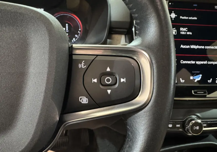 Gros plan sur le côté droit du volant noir en cuir du Volvo XC40 Recharge T5, avec commandes multifonctions et écran tactile visible.
