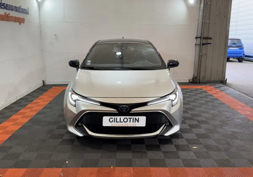 Vue avant frontale de la Toyota Corolla Hybride 122h Collection gris clair avec calandre noire et phares LED allumés.