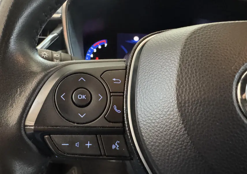 Gros plan sur le volant cuir noir de la Toyota Corolla Hybride 122h, avec commandes multifonctions et affichage digital partiel.