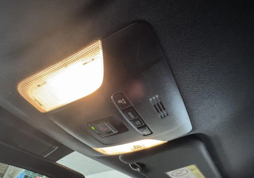 Plafonnier intérieur allumé avec commandes d’éclairage et téléphone, vue du toit d’une Toyota Corolla hybride gris clair.