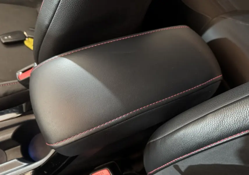 Détail de l'accoudoir central en cuir noir avec surpiqûres rouges dans l'habitacle d'une Toyota Corolla hybride.