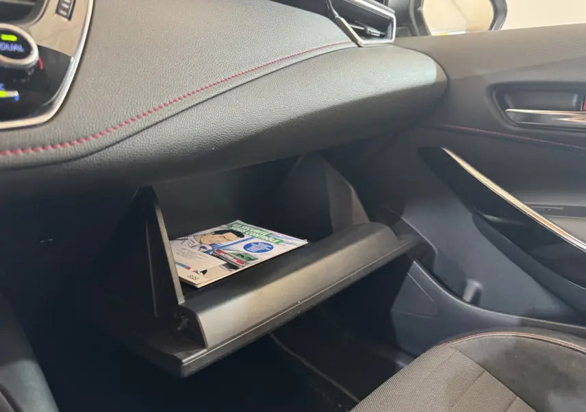 Intérieur côté passager de la Toyota Corolla hybride 2021, boîte à gants ouverte avec livret visible, sellerie noire.