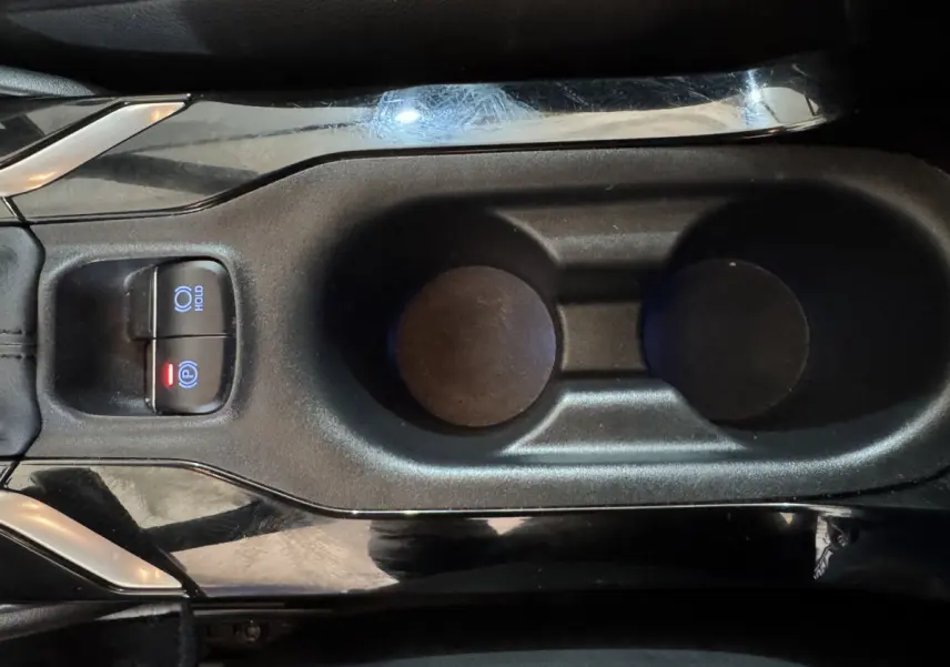 Vue rapprochée de la console centrale noire de la Toyota Corolla Hybride 122h avec boutons frein à main électrique et hold.