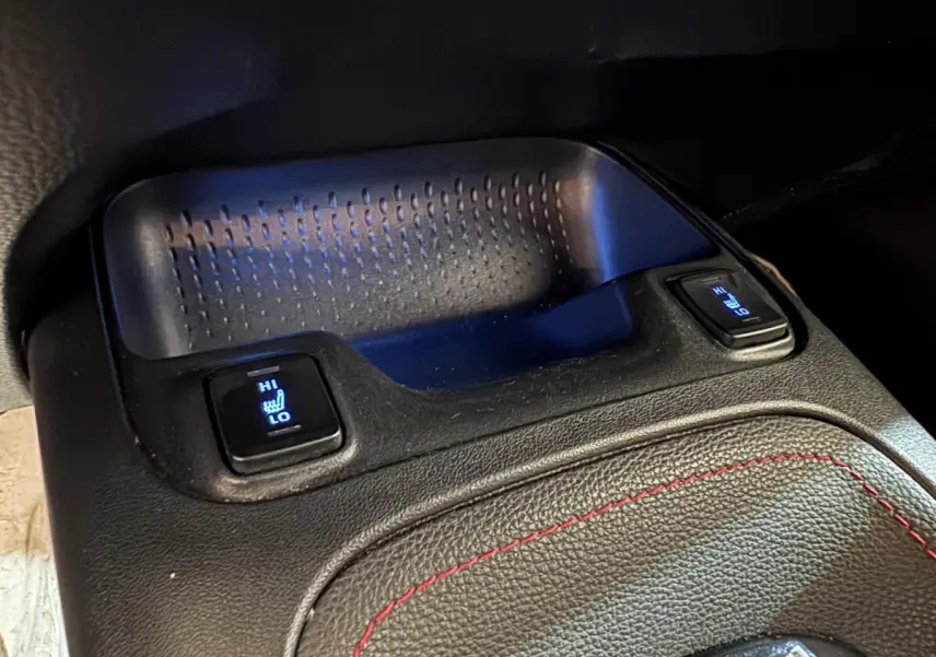 Gros plan sur les commandes de sièges chauffants avant, console centrale en cuir noir avec surpiqûres rouges, Toyota Corolla hybride.