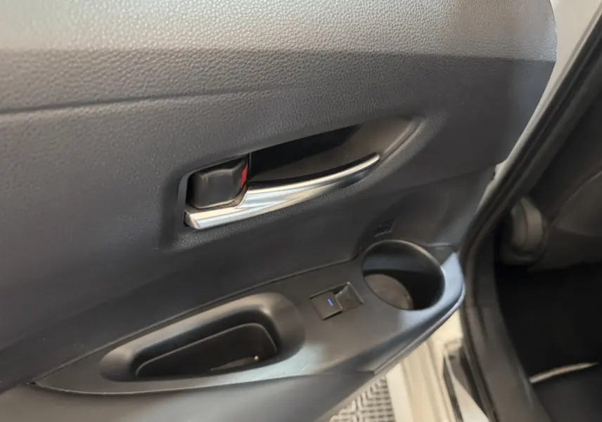 Gros plan sur la poignée intérieure et la commande de vitre de la porte avant gauche d'une Toyota Corolla hybride gris clair.
