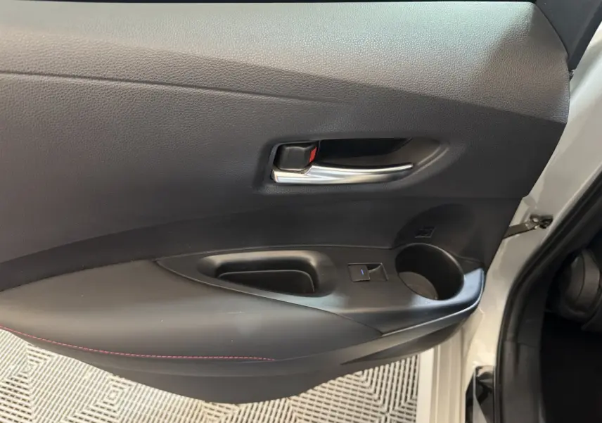 Vue rapprochée de la porte avant gauche grise de la Toyota Corolla Hybride 122h, avec poignée intérieure chromée et accoudoir noir.