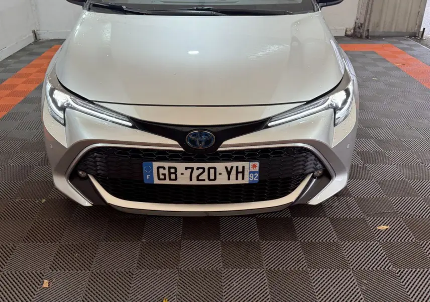 Vue avant rapprochée d'une Toyota Corolla Hybride 122h Collection gris clair avec calandre noire et phares LED fins.