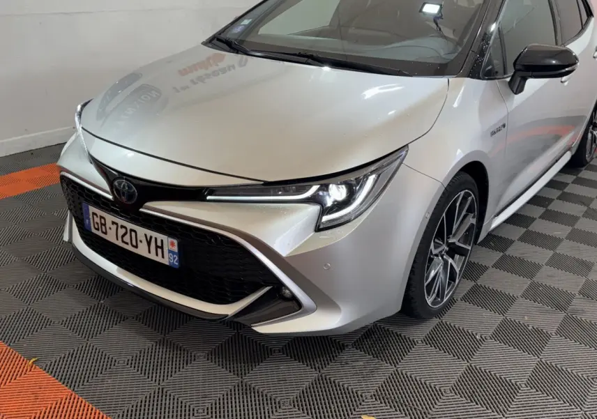 Vue 3/4 avant droit d'une Toyota Corolla Hybride 122h Collection gris clair avec phares LED allumés et jantes alliage.