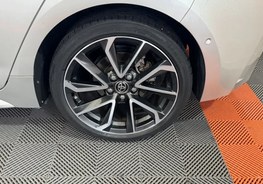 Gros plan sur la roue arrière droite gris clair d'une Toyota Corolla Hybride 122h Collection avec jante alliage noire et argent.