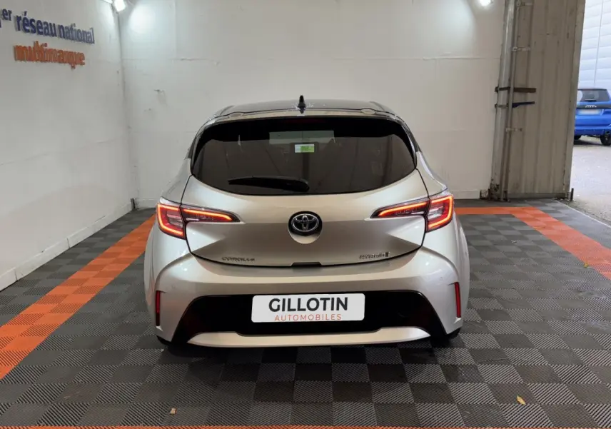 Vue arrière d'une Toyota Corolla Hybride gris clair avec feux LED allumés dans un garage.