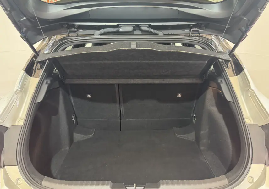 Coffre ouvert d’une Toyota Corolla hybride gris clair, vue arrière montrant l’espace de chargement vide et la tablette cache-bagages.