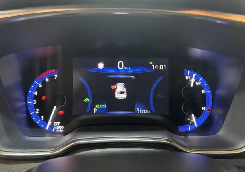 Vue rapprochée du tableau de bord numérique de la Toyota Corolla Hybride 122h gris clair, affichant 0 km/h et 71232 km.