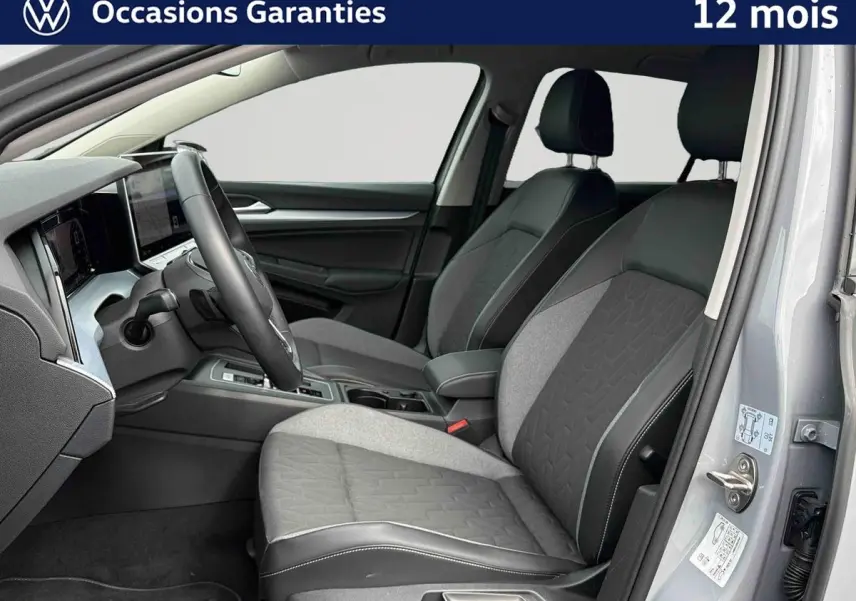 Intérieur avant droit d'une Volkswagen Golf grise 2025, sièges bi-matière gris et noir avec coutures apparentes.