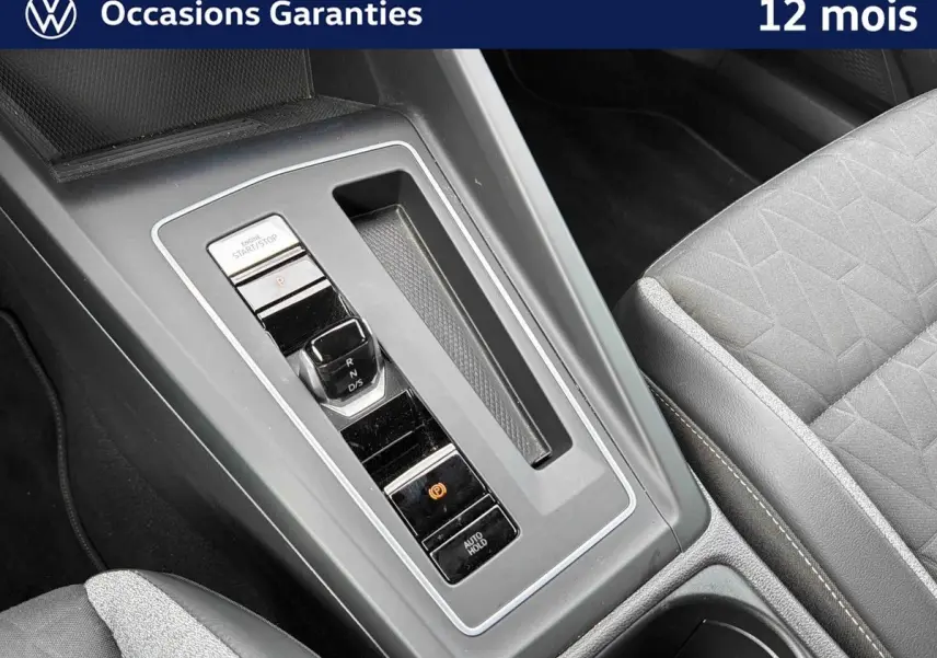 Gros plan sur la console centrale grise de la Volkswagen Golf 1.5 eTSI 2025 avec levier de vitesses et siège tissu gris.