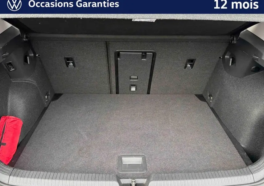 Coffre spacieux et propre d'une Volkswagen Golf 2025, vue de l'intérieur avec tapis gris et trousse de secours rouge.