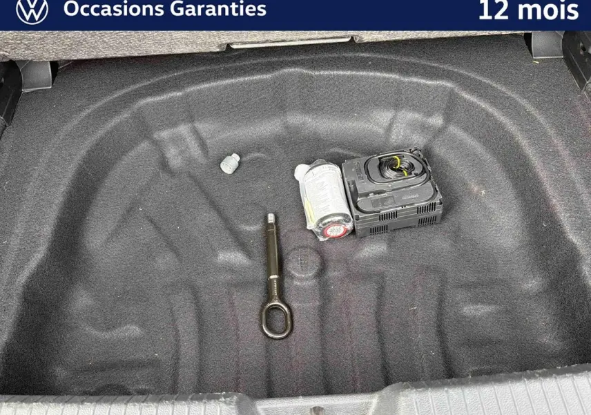 Vue plongeante sur le coffre ouvert d'une Volkswagen Golf grise, montrant un espace vide avec kit de réparation pneus.