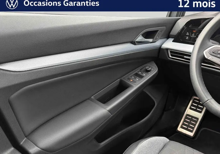 Intérieur côté conducteur de Volkswagen Golf gris, montrant la portière avec commandes électriques et partie du volant.