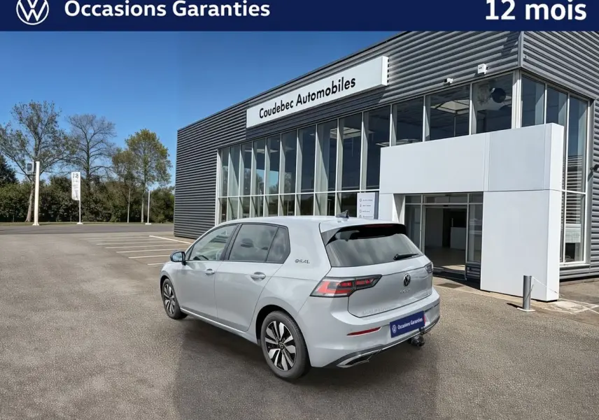 Vue 3/4 arrière droite d'une Volkswagen Golf grise stationnée devant un bâtiment moderne avec attelage escamotable visible.