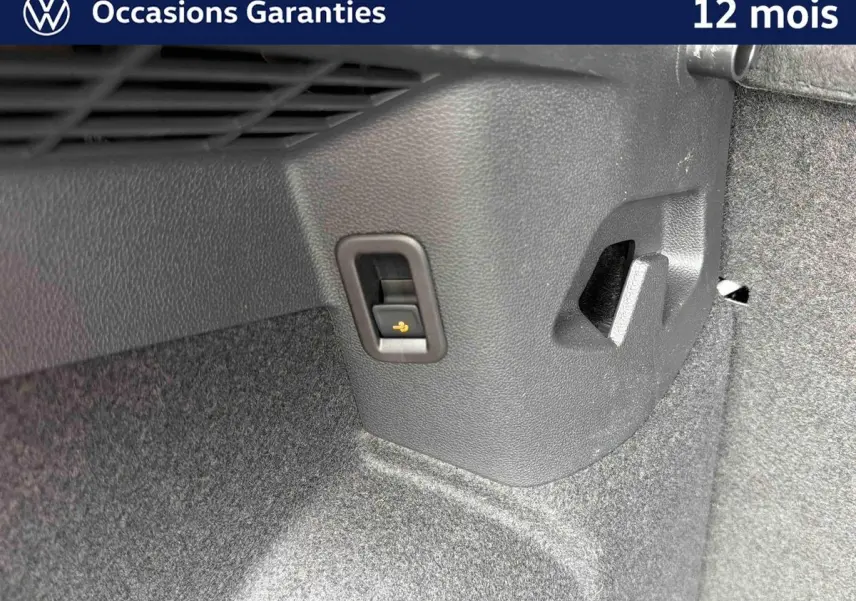 Détail du coffre d’une Volkswagen Golf grise montrant un levier de déverrouillage électrique du dispositif d’attelage.