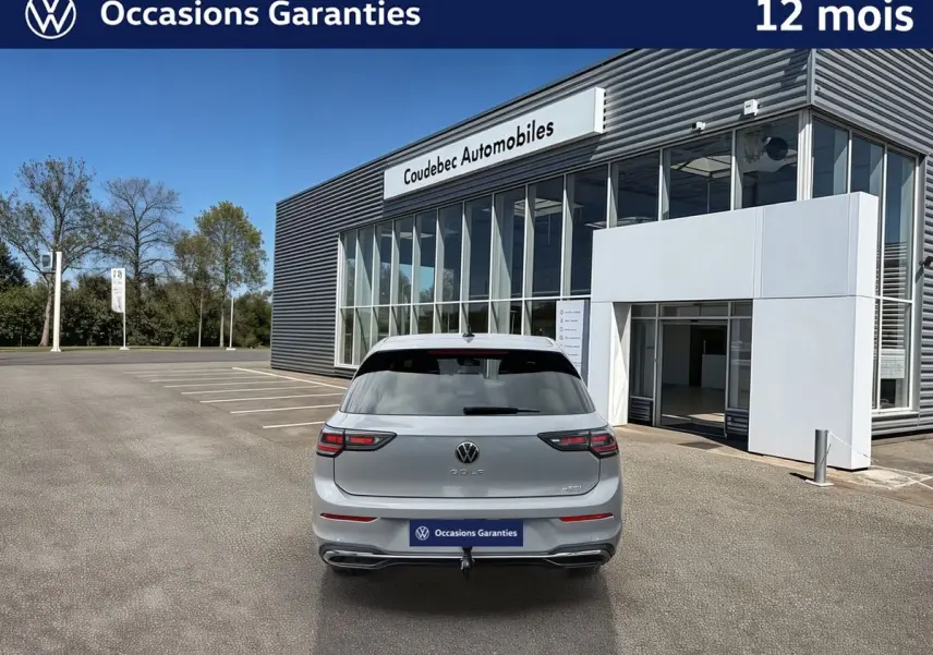 Vue arrière d'une Volkswagen Golf grise 2025 avec attelage escamotable, stationnée devant un bâtiment moderne.