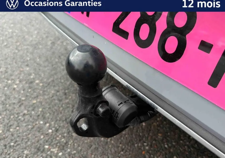 Gros plan sur l'attelage escamotable noir sous le pare-chocs arrière gris d'une Volkswagen Golf 2025.