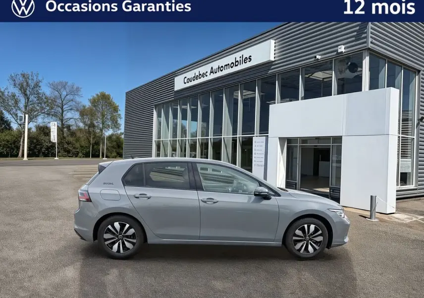 Vue latérale droite d'une Volkswagen Golf grise stationnée devant un bâtiment moderne en verre.
