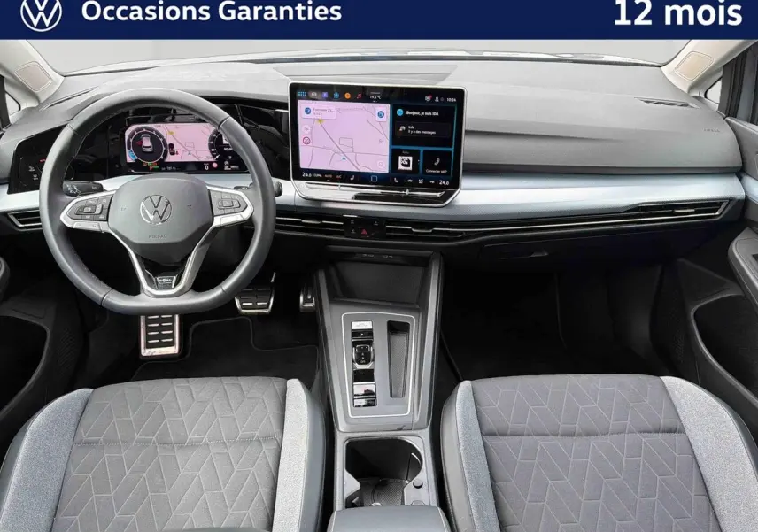 Vue intérieure avant de la Volkswagen Golf 1.5 eTSI 2025 avec tableau de bord digital et sièges gris à motifs géométriques.